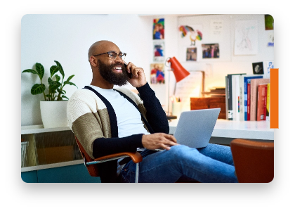A smiling man sits in a chair with a phone to his ear and a laptop on his lap representing an MS patient discussing MAVENCLAD® (cladribine) treatment with their doctor. Not a real patient.